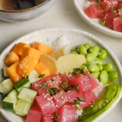 Fresh tuna poke bowl with diced vegetables and sesame seeds, served with soy sauce and side dishes.
