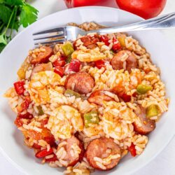 Savory shrimp and sausage jambalaya with rice, bell peppers, and tomatoes on white plate.