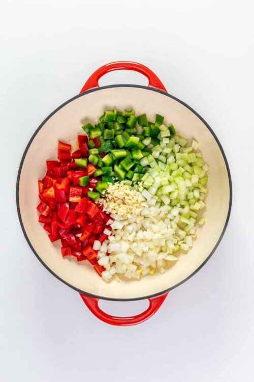 Chopped red bell peppers, green bell peppers, onions, and garlic in a white Dutch oven.