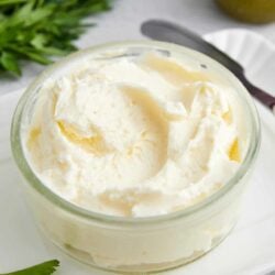 Creamy homemade butter in a glass jar with fresh herbs and a lime in the background.