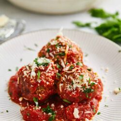 Savory Italian meatballs with marinara sauce, grated cheese, and herbs on a white plate.