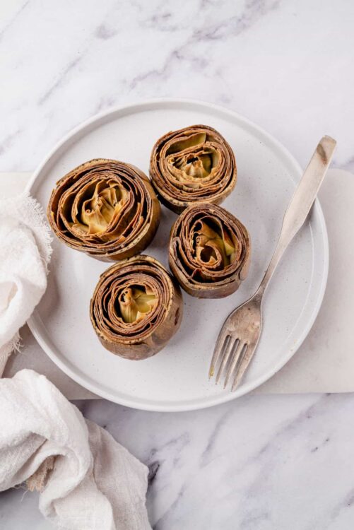 Roasted artichokes on a white plate with a vintage fork, perfect for healthy snack recipes.