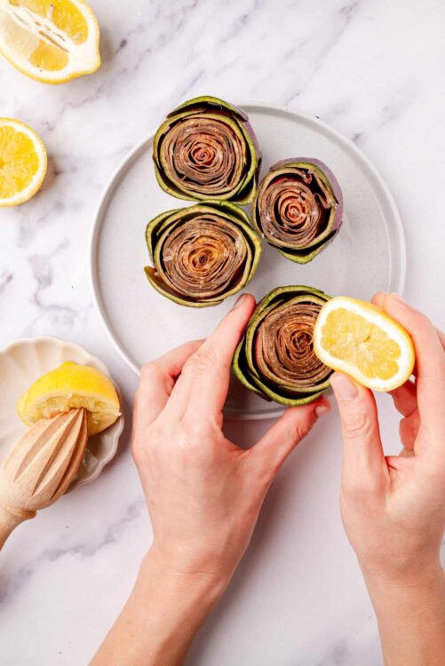 Roasted artichokes with lemon wedges on white plate.
