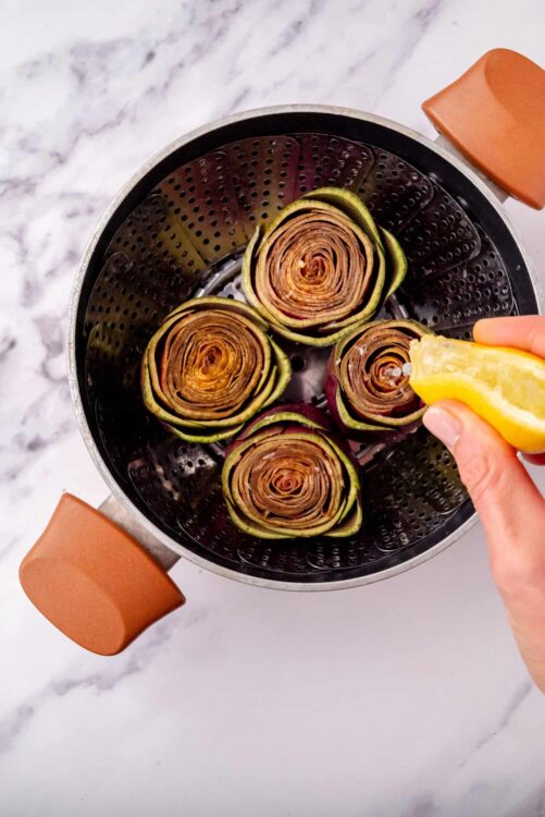 Roasted eggplant and zucchini roll-ups in a steam basket with lemon being squeezed.