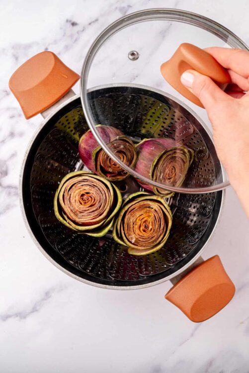 Roasted artichokes in a steamer basket preparing for baking or cooking.