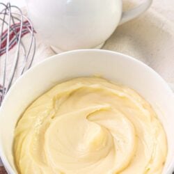 Creamy vanilla custard in a white bowl with a milk jug and whisk in the background.