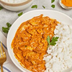 Creamy chicken curry with rice served on a white plate, garnished with fresh herbs.