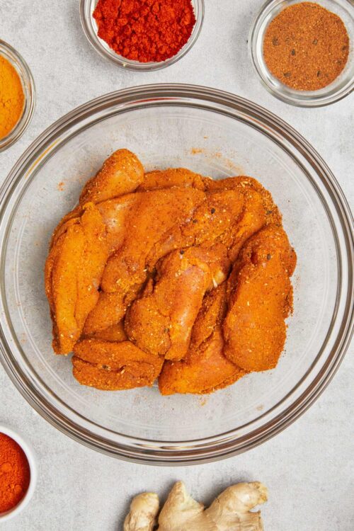 Seasoned chicken breasts with spices and herbs in a glass bowl.