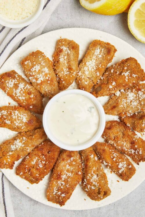 Crispy lemon chicken tenders with parmesan cheese and dipping sauce on a white plate.