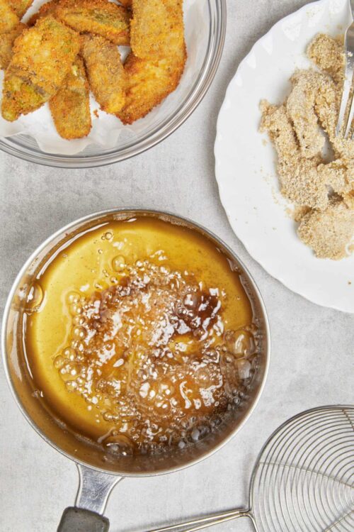Golden fried chicken in a glass dish, breaded chicken pieces on a white plate, and a sauce mixture in a stainless steel saucepan.