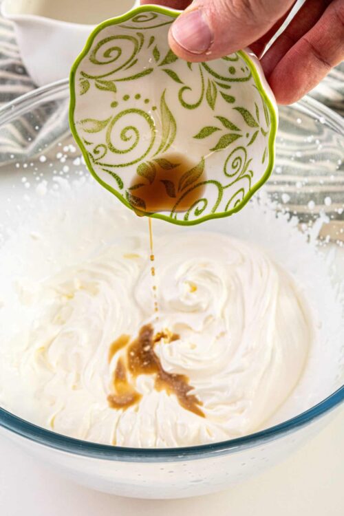 Flavored syrup being added to whipped cream in a glass bowl for dessert.