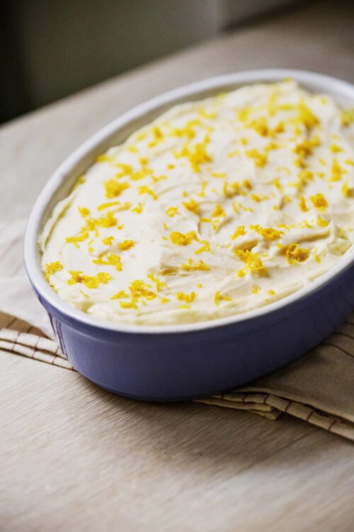Creamy lemon dessert with lemon zest sprinkles in a blue ceramic dish, served on a wooden surface.