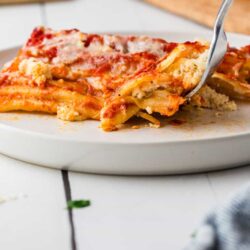 Delicious homemade lasagna with melted cheese and rich tomato sauce on a white plate.