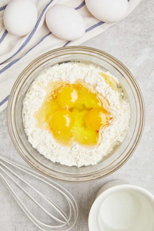 Creamy egg mixture with flour in glass bowl for baking recipe.