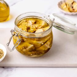 Canned artichokes in a glass jar with olive oil on a white marble surface.