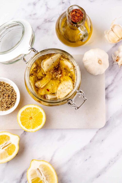 Marinated artichokes in olive oil with garlic, lemon, and herbs on marble countertop.
