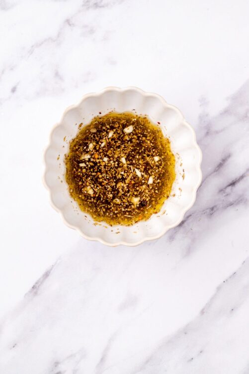 Minced garlic and chili oil in a small white bowl on marble surface.