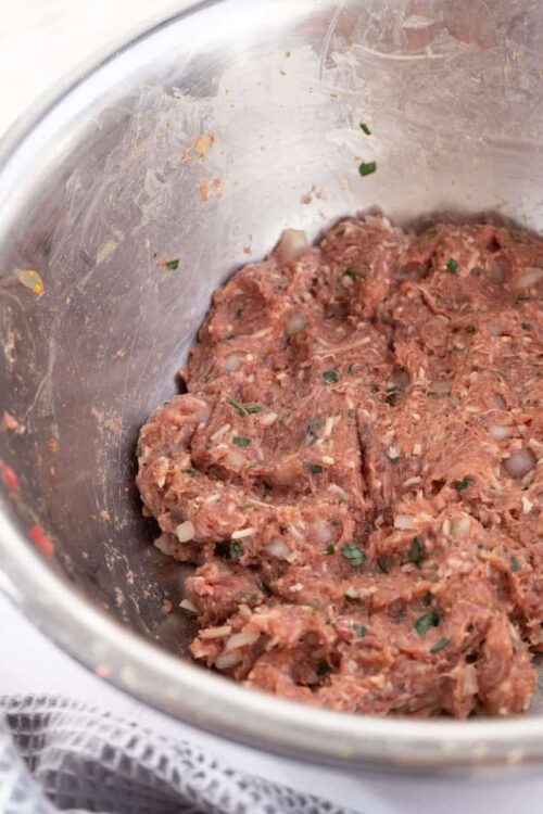Seasoned raw meat mixture for baking or cooking with herbs in a stainless steel bowl.
