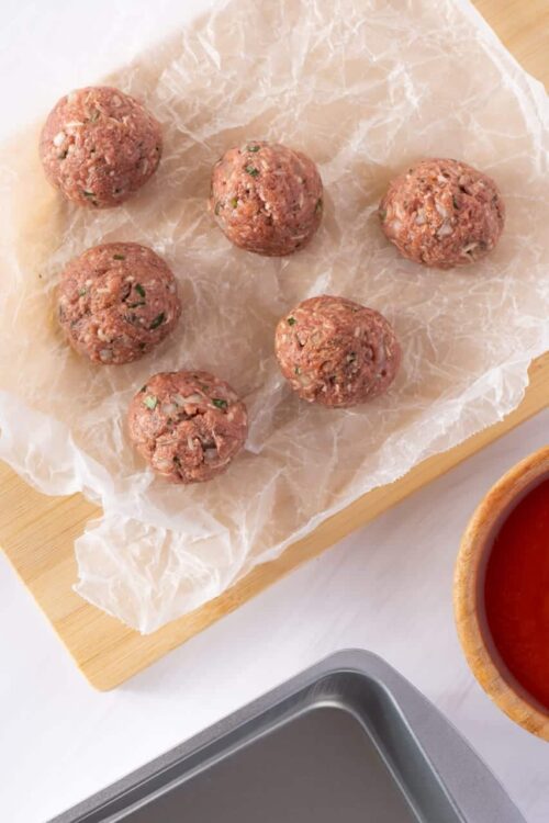 Seasoned meatballs on parchment paper for baking, ready to cook.