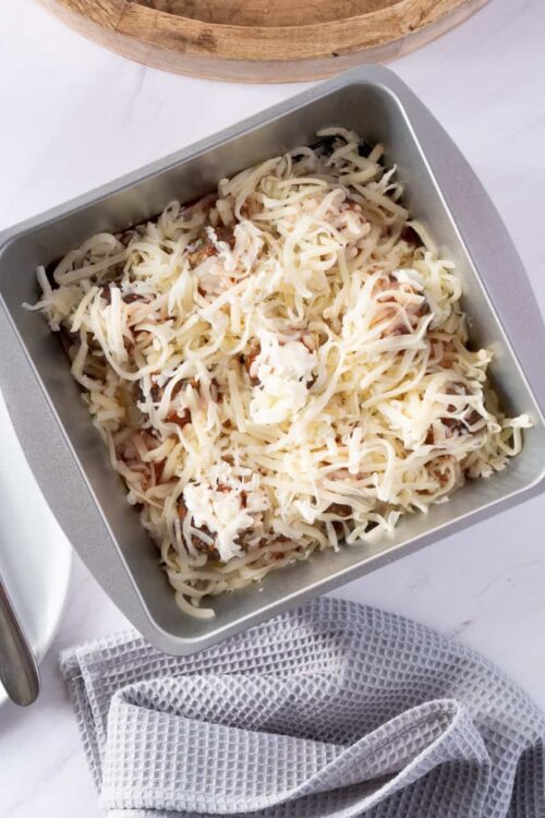 Cheeseburger casserole in baking dish with shredded cheese and cooked ground meat.