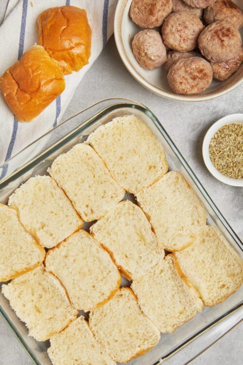 Soft bread slices ready for meatball sandwiches on a baking dish with ingredients background.