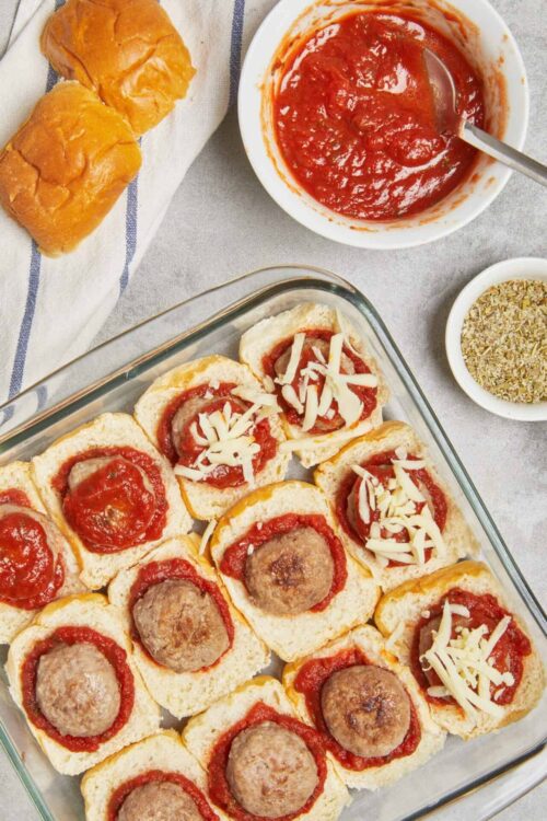 Baked meatball sliders with marinara and melted cheese in a glass baking dish.