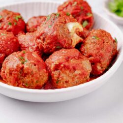 Juicy homemade meatballs in marinara sauce on white plate.