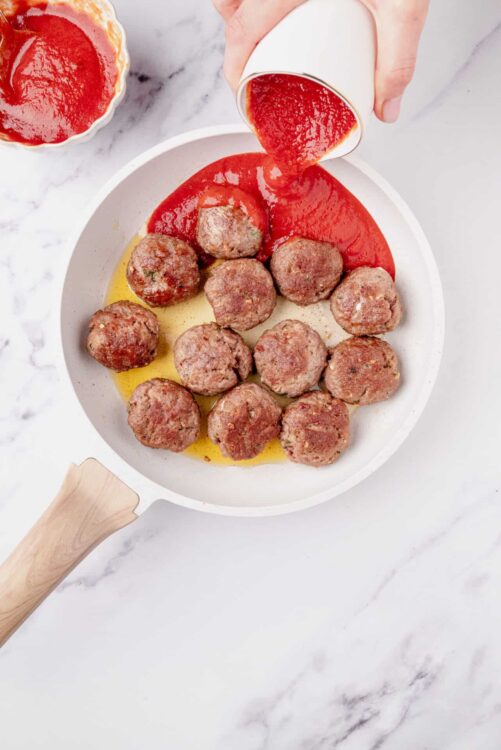 Juicy meatballs with marinara sauce in a white skillet. Cooking meatballs for homemade Italian dinner.