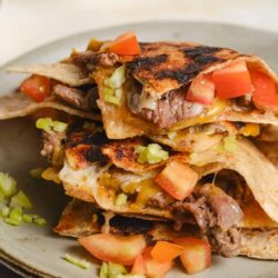 Crispy beef and cheese quesadillas filled with tomatoes and green onions on a ceramic plate.