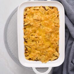 Crispy baked Nachos casserole with melted cheese in a white dish on gray background.