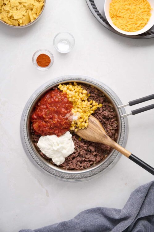 Ground beef with tomato sauce, corn, and sour cream in a skillet for beef taco filling.