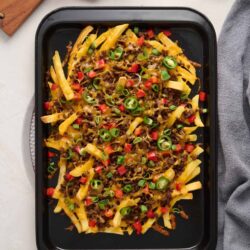 Crispy beef taco casserole baked in a black casserole dish with melted cheese, ground beef, and fresh chopped green onions on top.