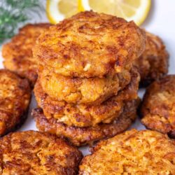 Golden crispy chicken patties with lemon slices and fresh herbs on white plate.