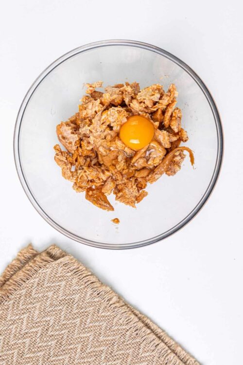 Eggs and shredded chicken mixture in a glass bowl on white background.