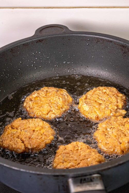 Crispy oatmeal cookies frying in a black skillet with hot oil.