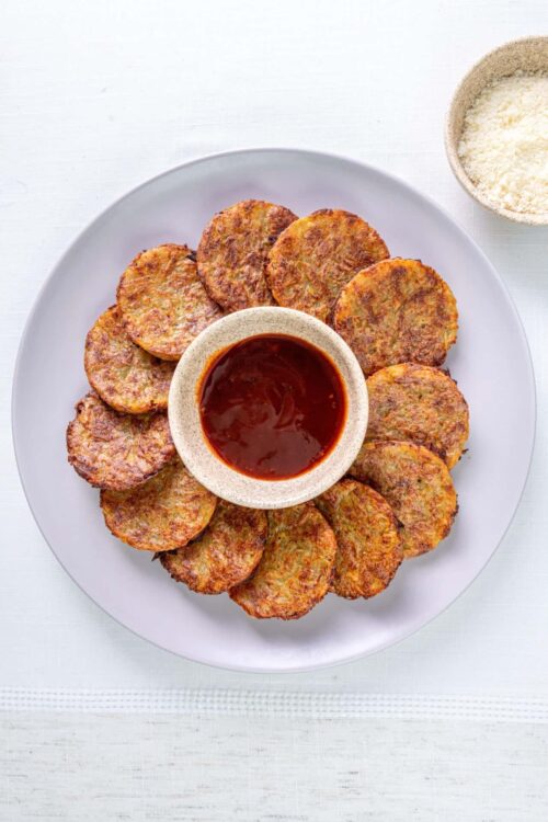 Crispy potato pancakes served with dipping sauce and grated cheese on the side.