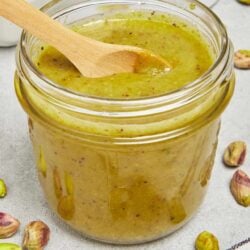 Creamy pistachio spread with a wooden spoon in a glass jar.