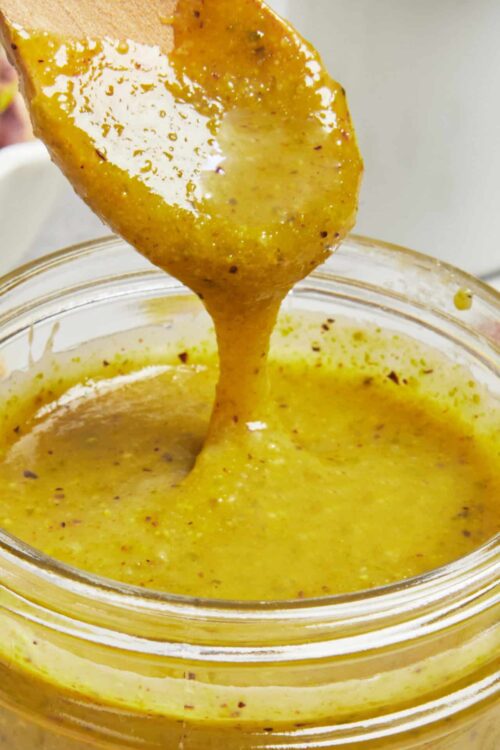 Golden mustard sauce pouring into jar, close-up of flavorful mustard condiment.