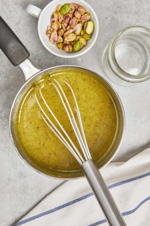 Creamy pistachio nut butter being mixed in a saucepan with a whisk.