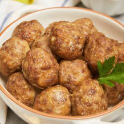 Savory meatballs in a white bowl with parsley garnish.