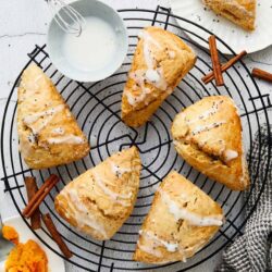 Golden flaky scones with glaze and poppy seeds, served on a cooling rack with cinnamon sticks on a white background.