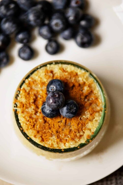 Fresh blueberry dessert with crumb topping in a glass jar, scattered blueberries nearby.