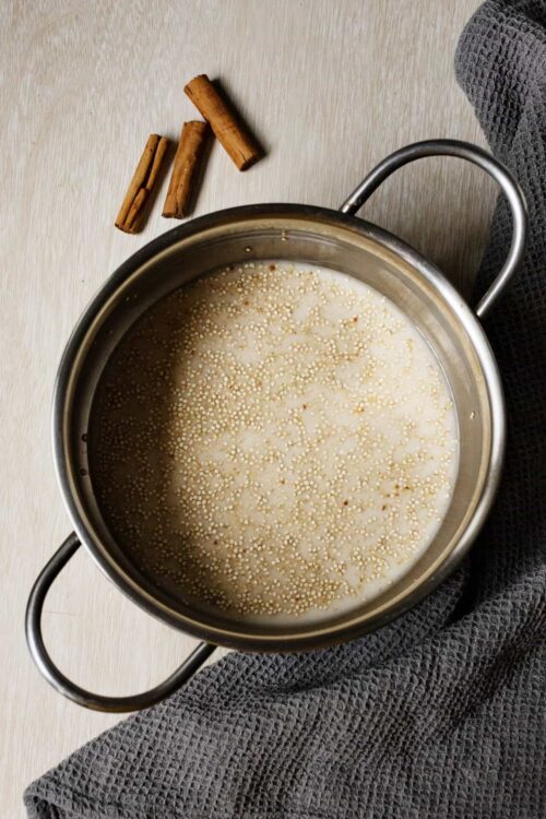Tiny cooking dahlia grains simmering in a pot of milk with cinnamon sticks nearby.