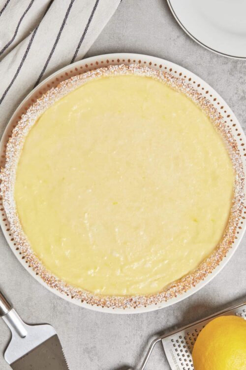 Lemon tart with a golden crust and glossy lemon filling on a white patterned plate.