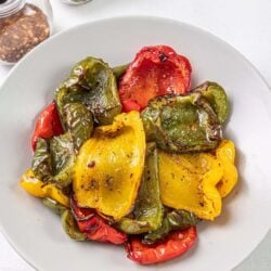Colorful roasted bell peppers on white plate with spices in background.