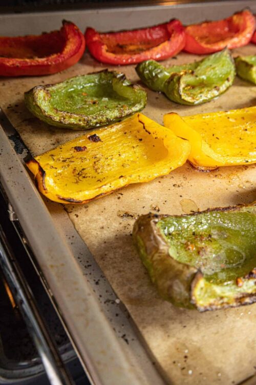 Roasted colorful bell peppers including red, yellow, and green on a baking sheet.