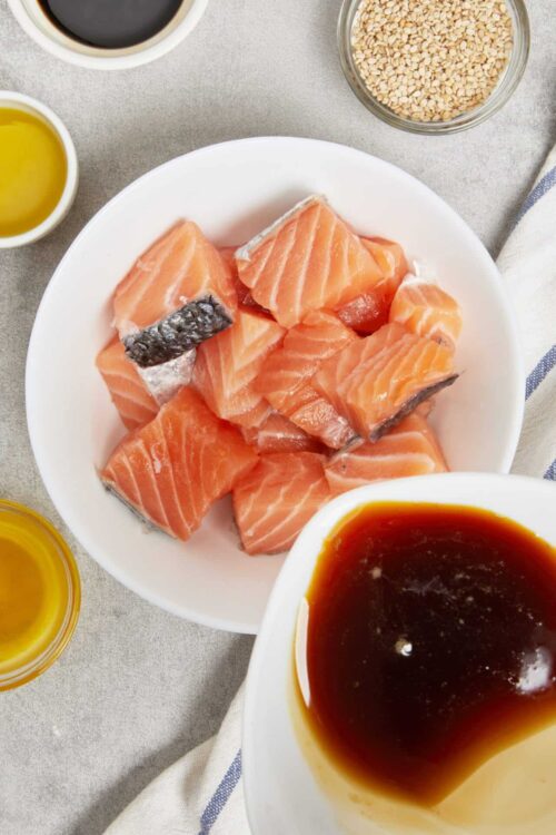 Fresh salmon fillets on a white plate with soy sauce and oil for sushi or cooking process, top view.