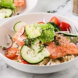 Fresh salmon and vegetable rice bowl with cucumber, cherry tomatoes, and avocado.