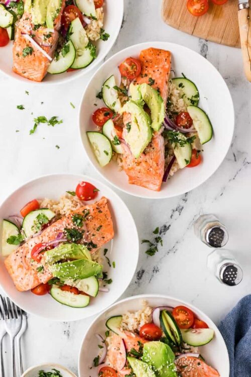 Fresh baked salmon with cucumber, cherry tomatoes, avocado, and herbs on a white plate, healthy and delicious seafood dinner.