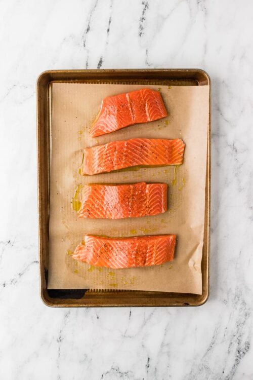 Fresh salmon fillets seasoned with oil and black pepper on a baking sheet. Perfect for baking or grilling.